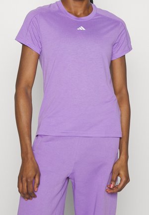 Gros plan d'une personne portant un t-shirt lavande à manches courtes et un pantalon assorti avec un petit logo blanc sur la poitrine.