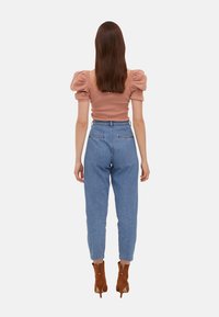 Puff-sleeved, fitted, rose-colored top paired with light blue high-waisted jeans. Brown ankle boots complete the outfit. Back view.