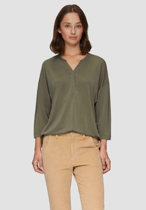 Haut olive à manches longues avec un col en V, doté de manches amples et d'un tissu doux et lisse, associé à un pantalon en velours côtelé beige.