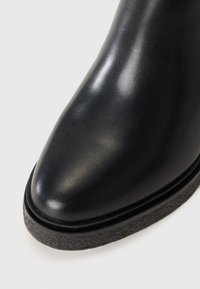 Botte de cheville en cuir noir avec un bout rond, texture lisse, semelle en caoutchouc basse avec un bord texturé. Pas de matériel ou d'ornements visibles.