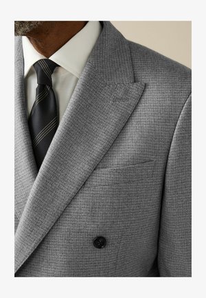 Gray double-breasted suit jacket with checked pattern, peak lapels, and a black button. Accompanied by a white shirt and a black tie with gold stripe.