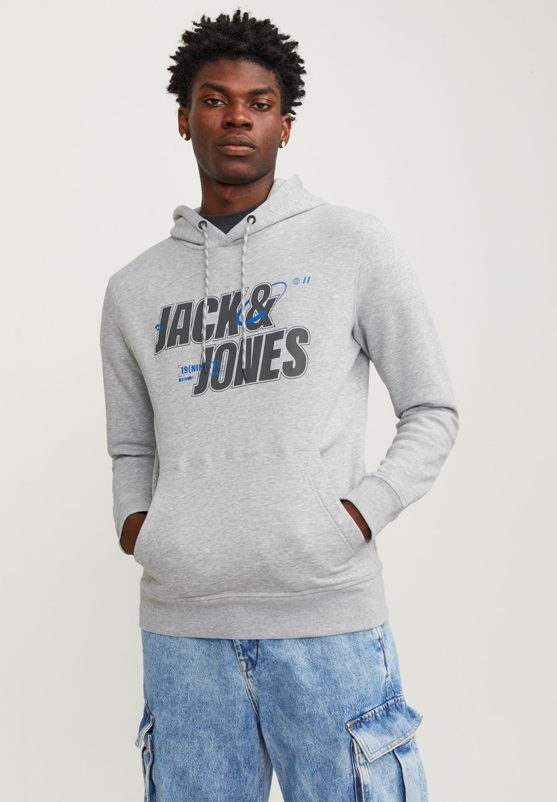 Sudadera gris con un bolsillo frontal, que presenta un gran texto gráfico en negro y azul "JACK & JONES". La tela tiene una textura suave y un ajuste relajado.