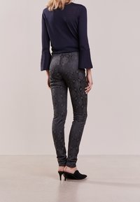 Svarta leggings med mönster i en texturerad ormsskinsdesign, kombinerat med en marinblå topp med trumpetärmar. Svarta klackskor.