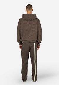 Hoodie marron à côtes avec poche kangourou et poignets ajustés, associé à un pantalon de jogging assorti avec une bande latérale crème.