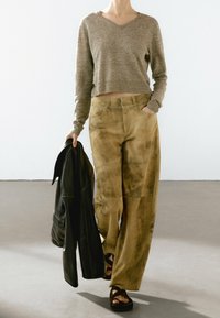 Haut court à manches longues beige associé à un pantalon large kaki avec une finition texturée. Modèle tenant une veste en cuir noir.
