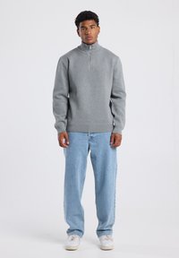 Gray pullover sweater with a half-zip collar, ribbed hem, and long sleeves, paired with light blue loose-fitting jeans and white sneakers.