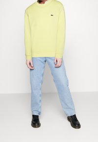 Gul tröja med rund halsringning och manschetter, kombinerad med ljusblå raka jeans och svarta snörkängor.