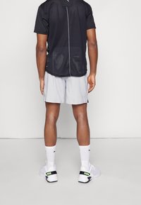 Czarna siateczkowa koszulka sportowa z krótkimi rękawami, w połączeniu z jasnoszarymi szortami. Białe trampki z czarnymi i zielonymi akcentami.