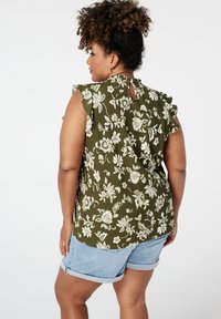 Groene bloes met bloemenprint, met ruche mouwen, van textuurstof en een sleuteltje in de rug, gedragen met lichte denim shorts.