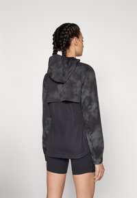 Schwarze Batikjacke mit Kapuze, die eine taillierte Taille und lange Ärmel hat. Weicher Stoff, leichtes Material und lockere Passform.