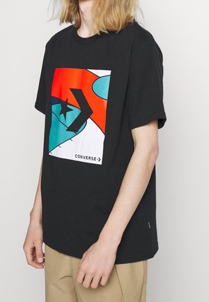 Zwarte t-shirt met korte mouwen met een kleurrijke grafische print in rood, blauw en wit met een stervorm en de tekst "CONVERSE" onderaan.