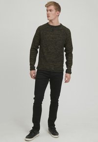 Mørkegrønn teksturert sweatshirt med lange ermer og rund hals, kombinert med svart slim-fit jeans og svarte joggesko.