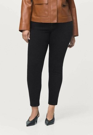Chaqueta de cuero marrón, vaqueros ajustados negros y zapatos de tacón negros. Los vaqueros tienen un corte slim y una textura suave, combinados con un diseño de chaqueta elegante.