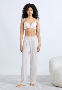 Bralette color beige chiaro abbinato a pantaloni da pigiama leggeri con righe verticali chiare. I pantaloni hanno una cintura elastica e una vestibilità ampia.