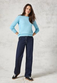 Helles blaues Strickpullover mit Rundhalsausschnitt, kombiniert mit dunkelblauen weiten Jeans und schwarzen Sneakers mit weißen Schnürsenkeln.