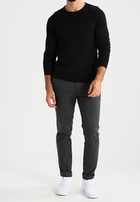 Zwarte langemouwen shirt, grijze slim-fit broek en witte sneakers. Katoenen materiaal, ronde halslijn, getailleerd ontwerp, opgerolde manchetten bij de broek.