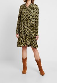 Svart klänning med gult blommönster, långa ärmar, krage och lätt utsvängd kjol. Matchad med bruna mocka cowboykängor.