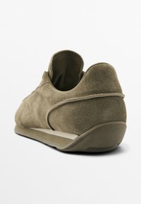 Grüner Wildlederschuh mit glatter Textur, niedrigem Profil und Gummisohle. Verfügt über minimale Nähte und eine schlanke Rückansicht.