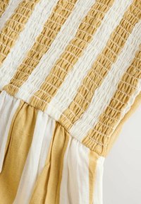Tissu rayé jaune et blanc présentant des points de smocks texturés et des plis froncés, créant une apparence superposée et une profondeur visuelle.