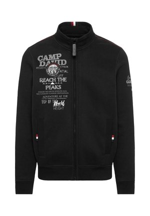 Schwarze Zip-Jacke mit hohem Kragen. Verfügt über aufgedruckten Text und ein Abzeichen auf der Vorderseite, kontrastierender Naht und gerippten Bündchen.