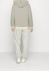 Beżowa bluza w paski z kapturem, zestawiona z jasnoszarymi spodniami dresowymi. Całość uzupełniają białe buty z delikatnym logotypem.