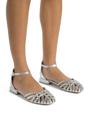 Sandales métalliques argentées avec un design à bout ouvert, présentant des sangles croisées, un talon plat et une sangle de cheville avec un détail de boucle. Texture lisse.