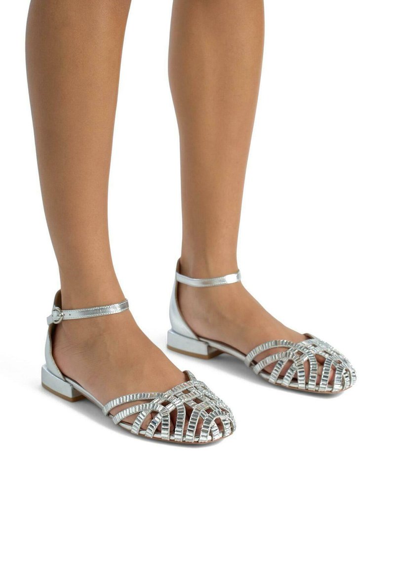 Srebrne metaliczne sandały z otwartym noskiem, z krzyżującymi się paskami, płaskim obcasem i paskiem na kostkę z zapięciem. Gładka tekstura.
