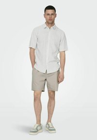 Lysstribet kortærmet skjorte i hvid og grå, parret med beige shorts og grå sneakers med kremfarvede accenter. Enkel og afslappet design.