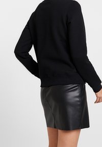 Svart sweatshirt med rund halsringning, åtsittande nederkant och långa ärmar, kombinerad med en svart läderminikjol, som visar mjuka texturer.