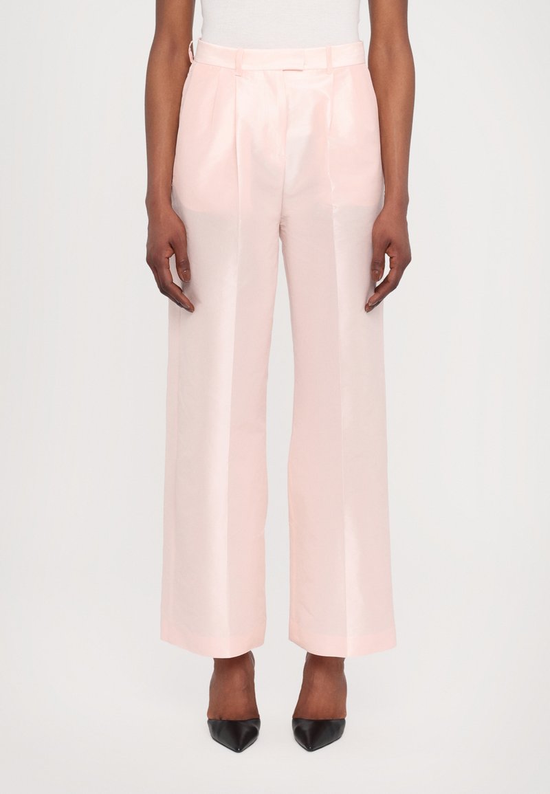 Light pink wide-leg trousers made of a glossy fabric, featuring front pleats and a fitted waistband, paired with black pointed-toe heels.