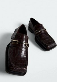 Mørkebrune læderloafer med krokodillelignende tekstur og guldfarvet metalspænde, firkantet tå, placeret på en lys overflade.