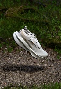 Hellgrauer Laufschuh mit atmungsaktivem Mesh-Obermaterial, strukturiertem Oberflächen, reflektierenden Akzenten und dicker Gummisohle.