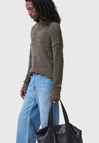 Olive green knitted sweater with textured finish, paired with light blue wide-leg jeans and a black leather tote bag.