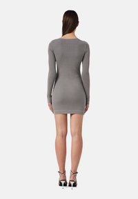 Robe grise côtelée à manches longues, présentant une silhouette ajustée et un col rond, se terminant au niveau des cuisses, associée à des talons noirs à lanières.