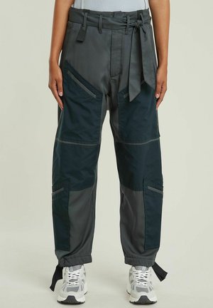 Cargo-Hosen aus dunkelgrauem und schwarzem Stoff mit einem Gürtel, mehreren Taschen und schmal zulaufenden Säumen. Texturierte Einsätze sorgen für visuelles Interesse.