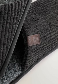 Mørkegrå tekstureret måtte med en ribbet overflade, prydet med en sort kant og en brun læderlogo-patch. Blødt indre materiale er synligt.