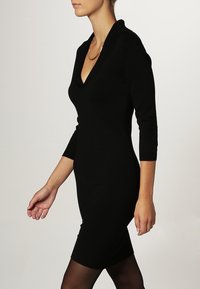Abito nero aderente con scollo a V, maniche a tre quarti e una texture liscia. Il design è elegante e sagomato sul corpo.