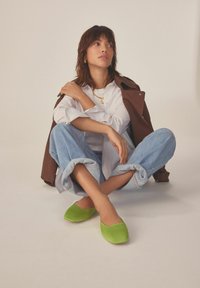 Zelené látkové boty na slip-on s nízkým střihem a béžovými akcenty, nošené s světle modrými džínami s vyhrnutými nohavicemi a bílou košilí.