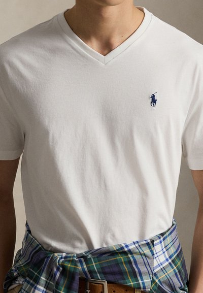 White cotton v-neck t-shirt with a navy polo logo on the left chest, paired with a blue and green plaid shirt tied around the waist.