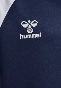Mörkblå sporttröja med vita detaljer och en framträdande Hummel-logotyp. Materialet verkar slätt med en lätt strukturerad yta.