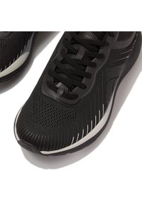 Schwarze Athletikschuhe mit einem atmungsaktiven Obermaterial aus Mesh, flachen Schnürsenkeln und weißen Akzenten entlang der Sohle und Seiten. Strukturiertes und stromlinienförmiges Design.