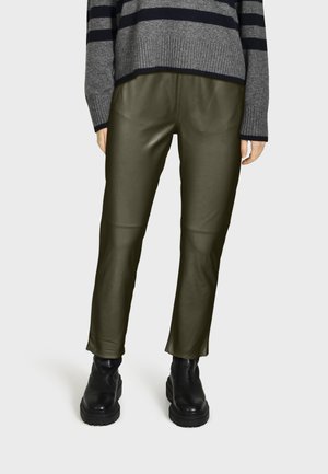 Pantalons en simili cuir vert olive avec une coupe slim, dotés d'un léger éclat et de détails de couture, associés à des bottines noires à semelle épaisse.