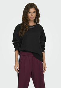 Zwarte oversized sweatshirt met een ronde hals en lange mouwen, gecombineerd met bordeauxrode tapered broek met zijstrepen.
