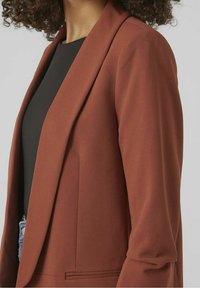 Rostbrun kavaj med en slät yta, slagkragar och en skräddarsydd passform. Har en enda framficka och ett fodrat inre.