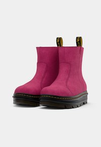 Bottines en suède rose avec une semelle extérieure noire côtelée, des coutures jaunes et deux languettes sur les bords supérieurs pour un enfilage facile.