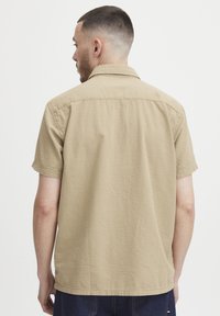 Korte mouw beige shirt van een gestructureerde stof, met een zachte kraag en een rechte zoom, van achteren getoond zonder zichtbare logo's of versieringen.