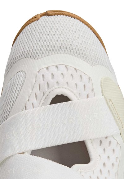 Witte sportschoen met ademend mesh bovenwerk, elastische band sluiting en een rubberen zool met bruine accenten.