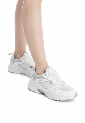 Zapatillas deportivas blancas con parte superior de malla, acentos texturizados y suela gruesa. Las características incluyen cordones, acolchado y detalle del logo.