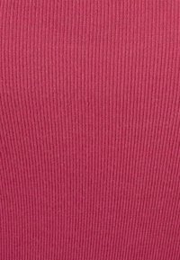 Tissu côtelé ajusté de couleur rose vif, présentant une surface texturée avec des rayures verticales et une apparence lisse.