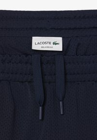Pantalones cortos azul marino con textura de malla, con una cintura elástica y cordones, etiquetados como "LACOSTE RELAXED FIT".